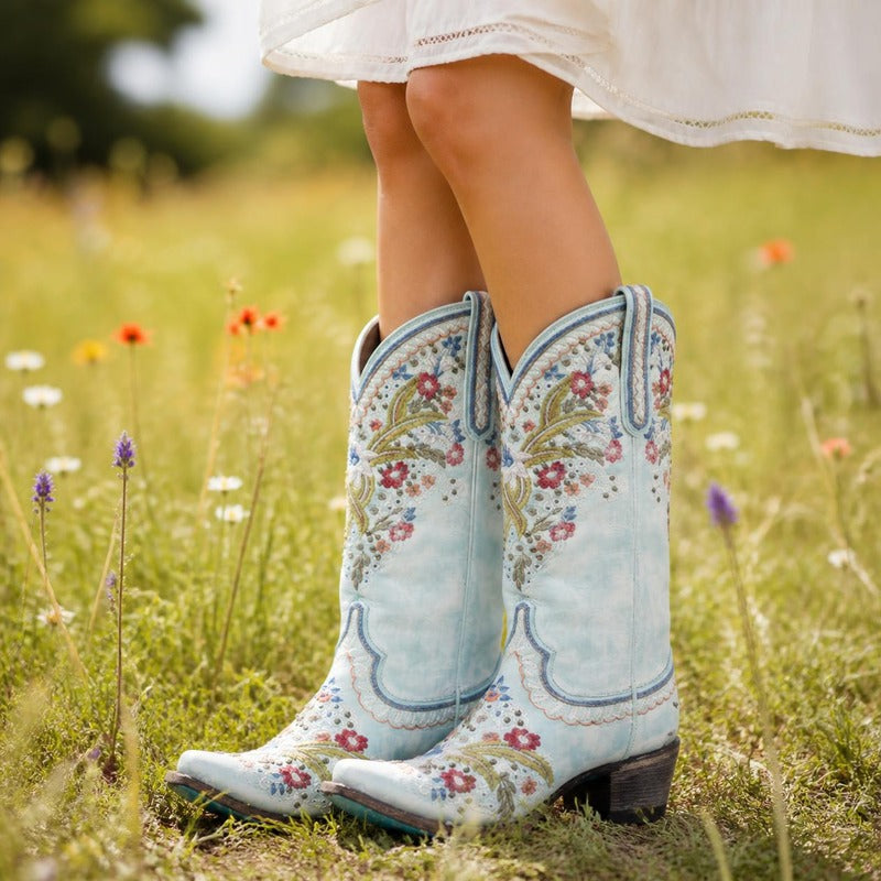 The Embroidered Western Boot in Ice Blue, worn in a meadow
